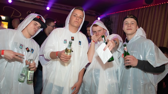 Vier Dudes in weißen Regenmänteln aus Plastik, mit Sputnik-Aufklebern und Bierflasche verziert.