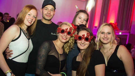 Ein Gruppe junger Menschen. Zwei Mädchen in der Mitte tragen rote 2019-Glitzerbrillen.